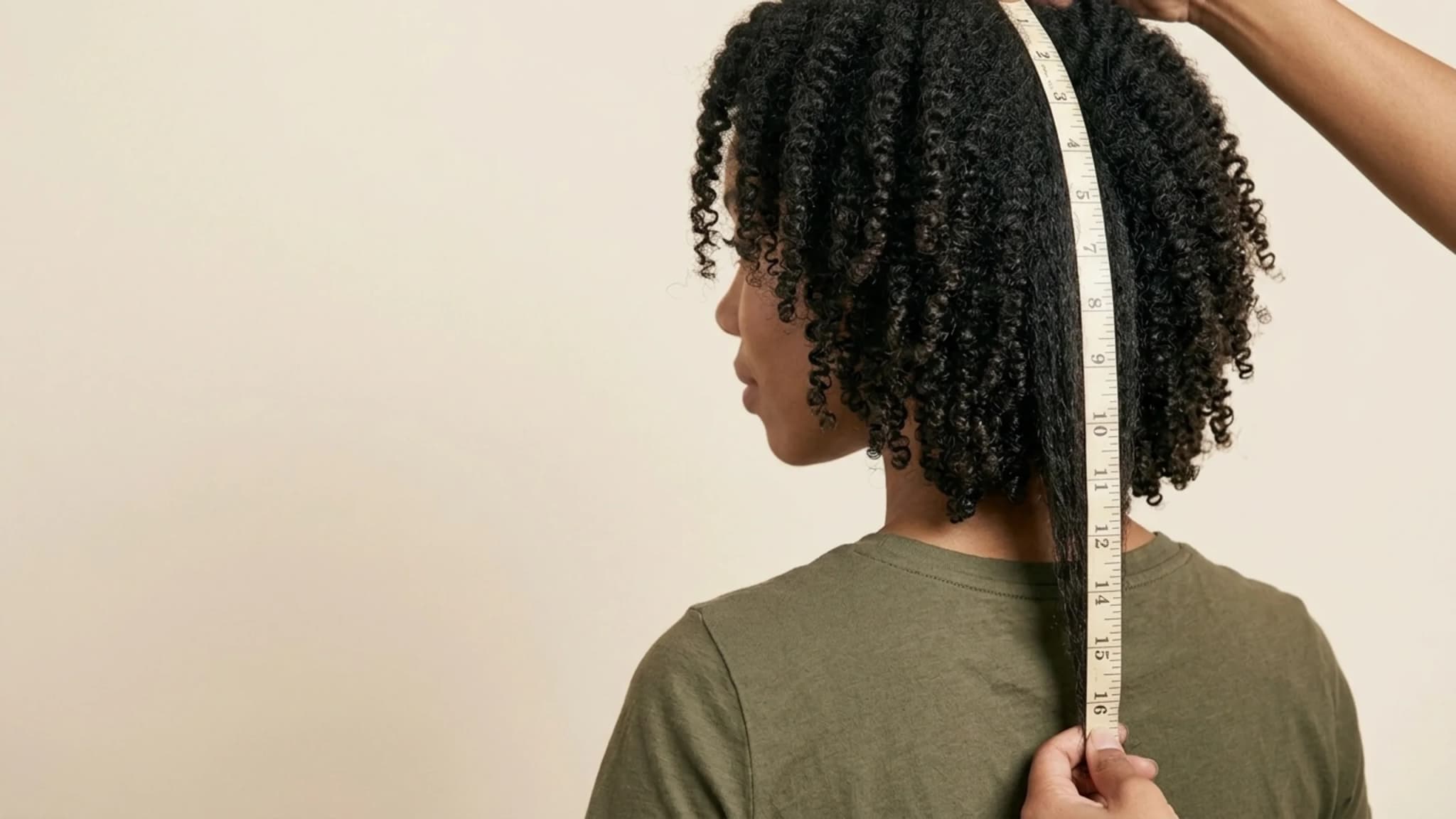 Woman with type 4 curls having a stretched section measured down her back with a tape measure