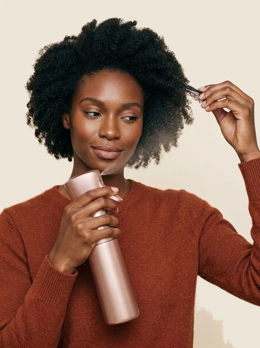 Woman misting a section of her coily hair with a pink spray bottle